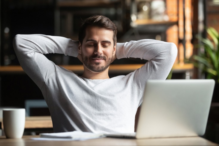 A person sitting at a table with a computer and smiling at the camera Description automatically generated