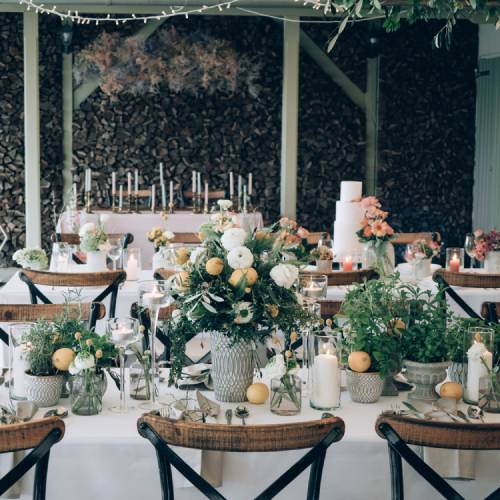 A beautifully decorated room with several tables lined with white table clothes, floral arrangements, and large candles.