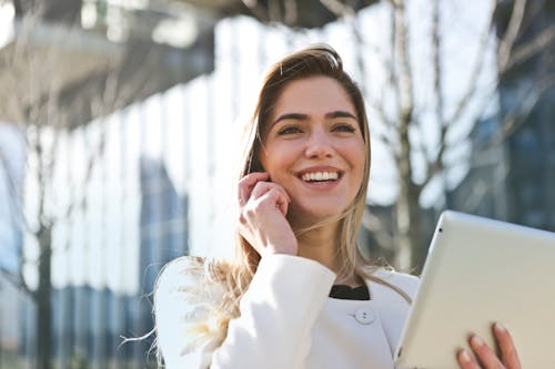 Free Confident businesswoman using her tablet and phone, smiling outdoors in sunlight. Stock Photo