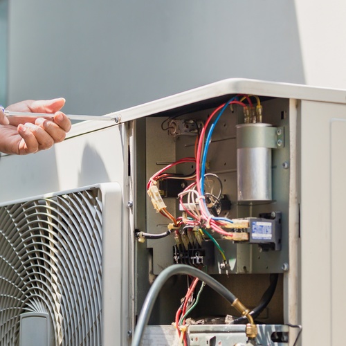 A close-up view shows a technician using a screwdriver to twist a screw on an outdoor AC unit.