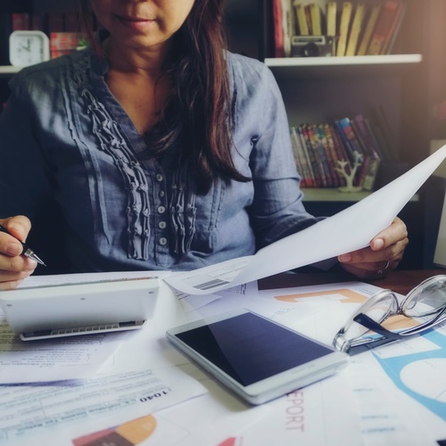 A woman sitting at her desk spending time retirement planning with paperwork and a small tablet in front of her.