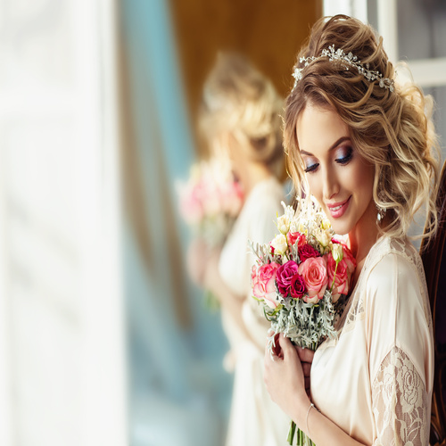 A beautiful bride with a wedding bouquet. A blonde woman with big, curly hair and fashionable event makeup.