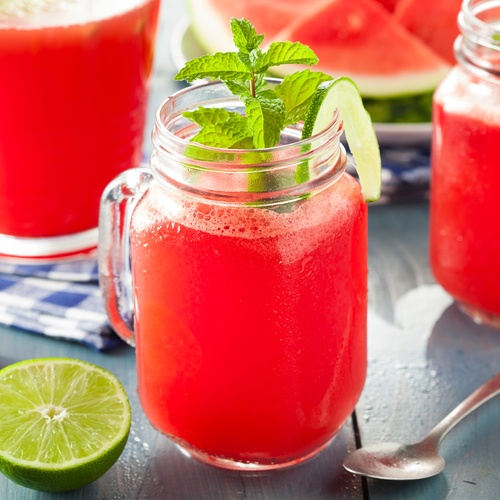 Three mason jar mugs full of bright red watermelon agua fresca. Lime slices and mint leaves accent each drink.
