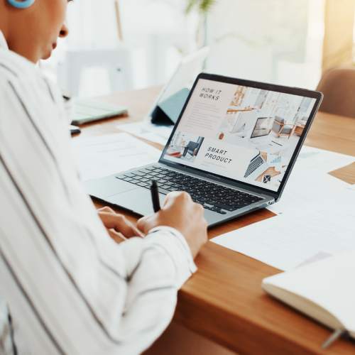A businesswoman notes while looking at her laptop in the office, planning, reminders, and product info.