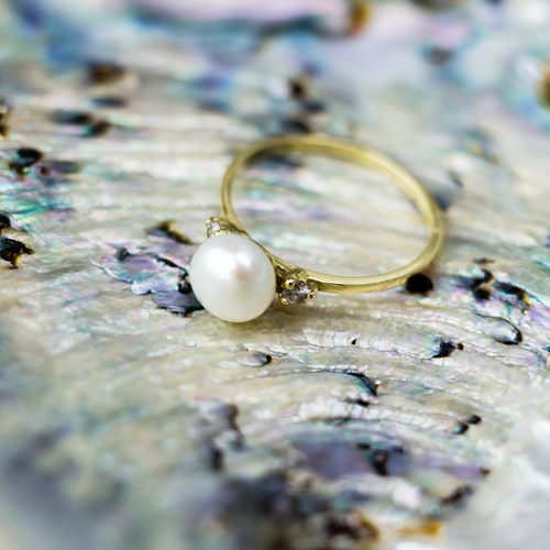 A vintage engagement ring with a pearl center and gold band is set against an iridescent shell background.